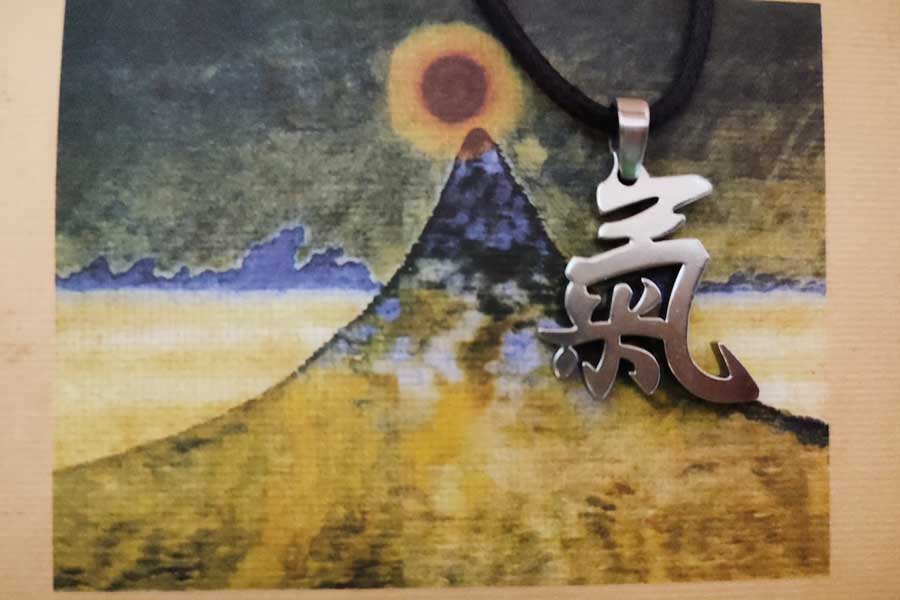 漢字の「気」の旧字体をかたどったペンダントトップ。背景には宮沢賢治作「日輪と山」木版画が【写真提供：ルカ・コッカロ】