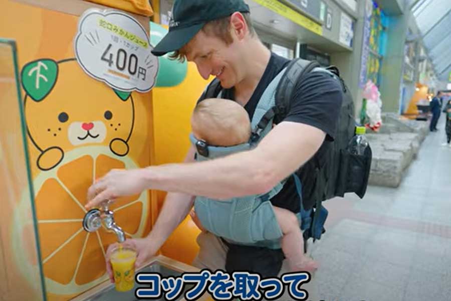 松山空港で「噂のミカンジュースの蛇口」に笑顔のジェイコブさん（画像はスクリーンショット）