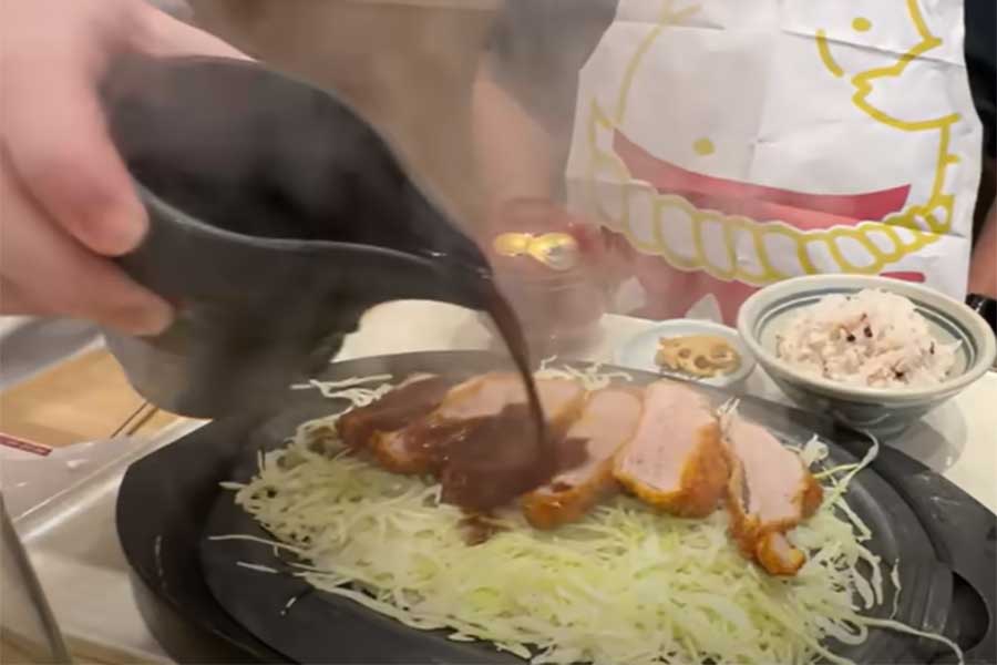 鉄板で用意されたトンカツと、そこへかけられた赤みそのソース（スクリーンショット）