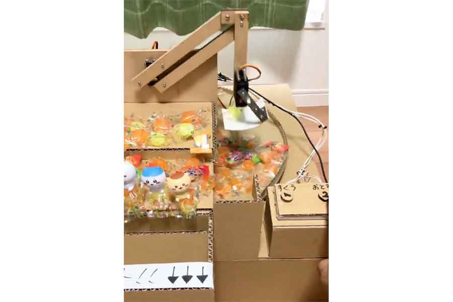 段ボールで自作したクレーンゲーム機。精巧に作られたアームでお菓子をすくっていく(スクリーンショット)